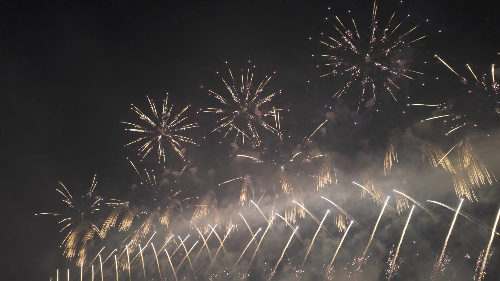 Multiple fireworks bursting above smoke at the Omagari National Fireworks Competition