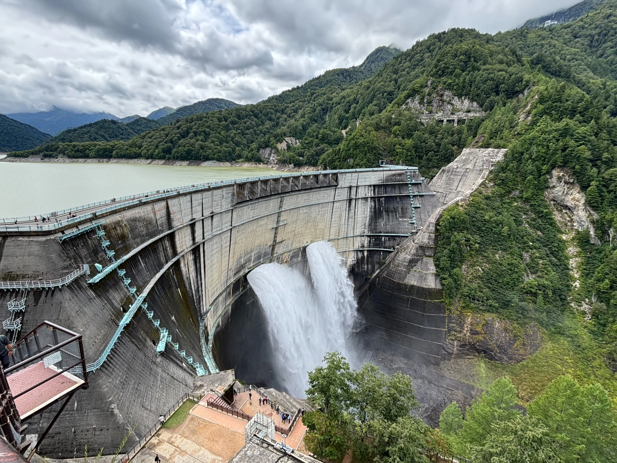 Water being discharged from Kurobe Dam beneath a cloudy mountain sky